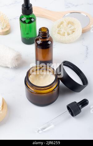 Vasetto crema idratante aperto ed essenziale o lozione in bottiglia di vetro ambrato e set di prodotti per la cura della pelle e del corpo su sfondo bianco. Confezioni cosmetiche Foto Stock