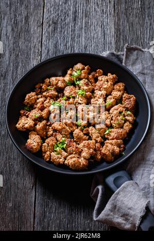 Salsiccia italiana fritta di carne di maiale appena macinata e spezie in padella su tavolo di legno scuro, vista verticale dall'alto Foto Stock