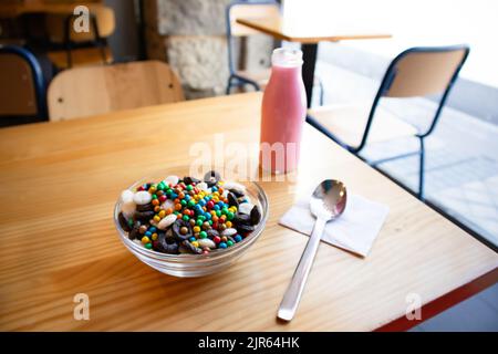 Colazione a secco in ciotola di vetro su un tavolo di legno nel caffè. Deliziosi cornflakes e latte rosa in una bottiglia. Colazione sana e utile. Cibo per Foto Stock