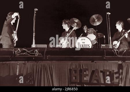I Beatles in scena al Gator Bowl di Jacksonville, Florida, il 11 settembre 1964. L'uragano Dora aveva colpito Jacksonville il giorno precedente e i venti forti rimasti, con una raffica di 45 miglia all'ora, richiesero che la batteria di Ringo Starr fosse inchiodata sul palco e che la scritta "Beatles" di cartone sul lato del palco fosse finalmente strappata via. (USA) Foto Stock