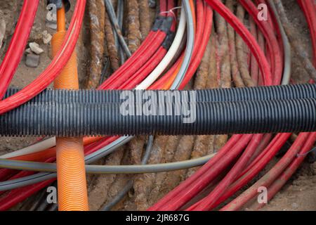 I cavi di rete in tubo corrugato rosso sono interrati nella strada. Installazione di infrastrutture di cavi elettrici sotterranei. Cantiere Foto Stock