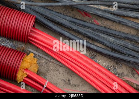 I cavi di rete in tubo corrugato rosso sono interrati nella strada. Installazione di infrastrutture di cavi elettrici sotterranei. Cantiere Foto Stock