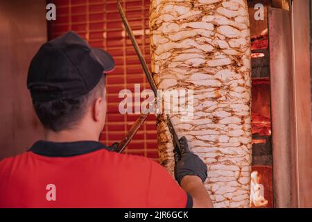 Lo chef prepara un kebab donatore tagliando fette di carne tostate dallo spiedino alla griglia in un ristorante fast food. Foto Stock