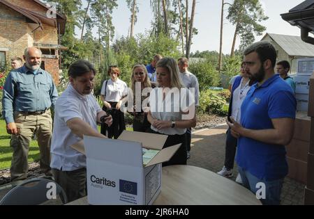 2022-08-22 10:24:42 i ministri olandesi del Commercio estero e dello sviluppo Liesje Schreinemacher (C) partecipano alla sua visita al centro collettivo della Caritas, che offre aiuti umanitari ai locali della città di Irpin, vicino a Kyiv, Ucraina, il 22 agosto 2022. I ministri olandesi del Commercio estero e dello sviluppo Liesje Schreinemacher e il ministro della Difesa Kajsa Ollongren visitano Kyiv e le città suraund per incontrare i funzionari ucraini. Irpin così come altre città e villaggi nella parte settentrionale della regione di Kyiv divenne campi di battaglia e furono pesantemente sgusciati quando le truppe russe tentarono di raggiungere la capitale Ucraina Kyi Foto Stock