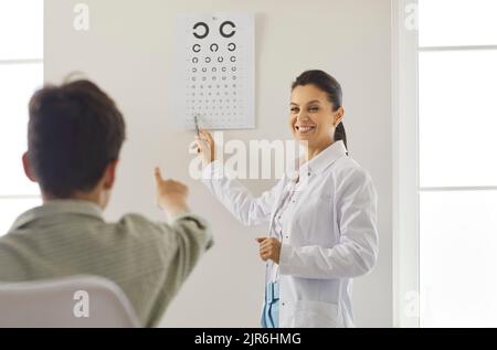 L'optometrista amichevole sta controllando la visione del ragazzo in ufficio di oftalmologia con l'aiuto della tabella di prova. Foto Stock