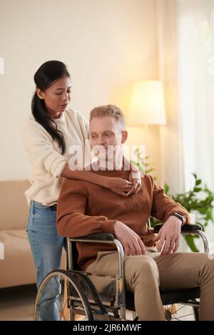 Giovane donna vietnamita in felpa beige che abbraccia il ragazzo in sedia a rotelle Foto Stock