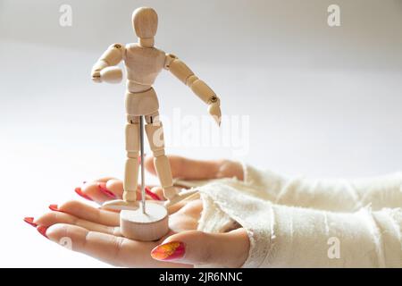 due mani femminili con polsi rotti dopo essere caduto da una bicicletta in un getto su uno sfondo isolato con manichino di legno di un uomo, mani in un ca Foto Stock