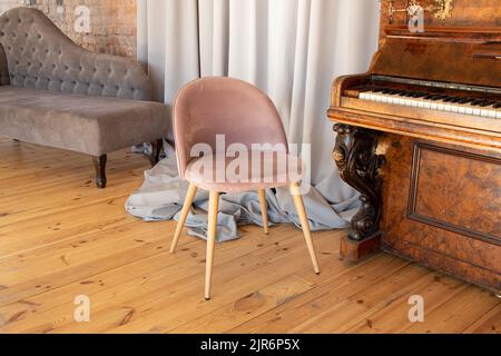 poltrona in velluto chiaro e morbido si trova vicino al pianoforte nell'appartamento, negli interni e nei mobili, nella casa Foto Stock