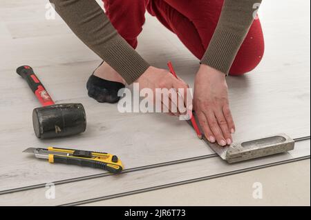 Il maestro femminile disegna una linea a matita sulla tavola, installando pavimenti in vinile al quarzo, lavori di installazione. Foto Stock