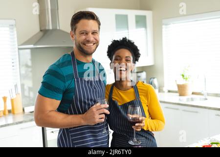 Immagine di felice coppia varia in grembiuli con vino in cucina Foto Stock