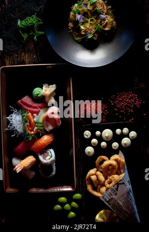 Tavolo del ristorante Fusion con piatti di varietà su sfondo di legno nero Foto Stock