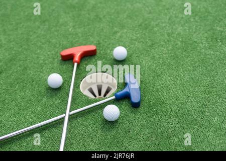 Putters e palle da golf in miniatura assortiti si inclinano su erba sintetica. Foto Stock