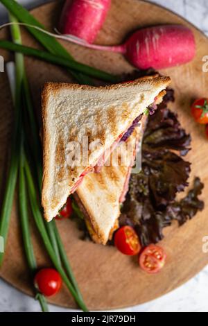 sandwich croccante succoso con prosciutto e verdure a bordo. Foto Stock