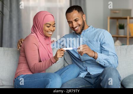 Concetto di paternità. Coniugi musulmani neri felici che tiene il test di gravidanza positivo nel paese Foto Stock