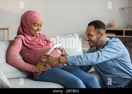 Musica di gravidanza. Cheerful Black Man posizionare cuffie wireless sul ventre di moglie incinta Foto Stock