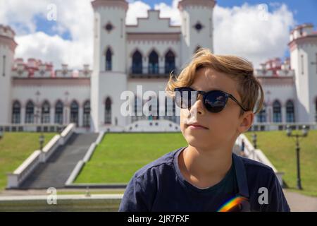 Bel ragazzo di 9 anni di stile posa con occhiali da sole e sorridente sull'antico castello in Bielorussia giovane turista che guarda le attrazioni storiche. Foto Stock