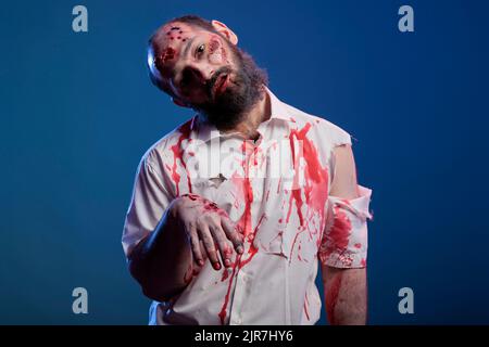 Spaventoso zombie non morti guardando male pazzo, avendo sangue sulla camicia e pericoloso aggressivo sanguinoso look. Cadavere apocalittico inquietante con cicatrici e ferite sporche brutte, cervello che mangia demone. Foto Stock