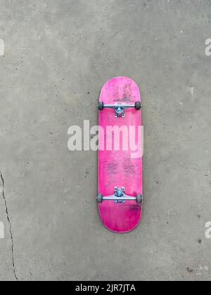 Scricchiolò su skateboard rosa che si posa su una superficie liscia in cemento presso lo skatepark locale Foto Stock