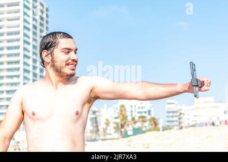 Un maschio felice in spiaggia che fa un selfie con uno smartphone Foto Stock