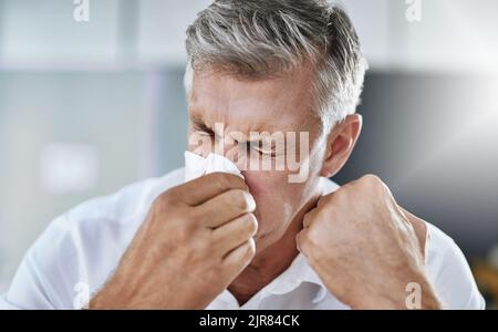 Le allergie non sono divertimento. Un uomo d'affari maturo che soffia il naso in ufficio. Foto Stock