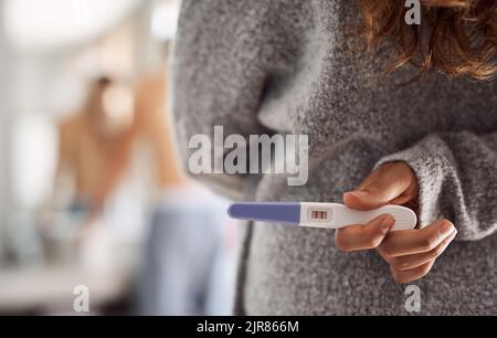 Questo potrebbe cambiare tutto. Una donna irriconoscibile che nasconde un test di gravidanza dietro la schiena in bagno. Foto Stock