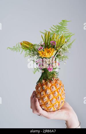 Alzati, indossa una corona, essere dolce all'interno. Foto da studio di una donna irriconoscibile che tiene un ananas su uno sfondo grigio. Foto Stock