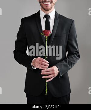 L'abbigliamento perfetto per i signori. Foto studio di un uomo ben vestito che tiene una rosa rossa su uno sfondo grigio. Foto Stock