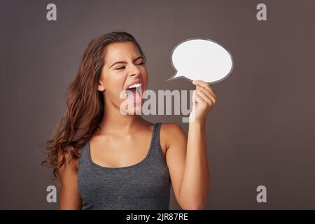 Voce forte per una donna forte. Studio shot di una giovane donna attraente che tiene una bolla di discorso in bianco e gridando su uno sfondo grigio. Foto Stock