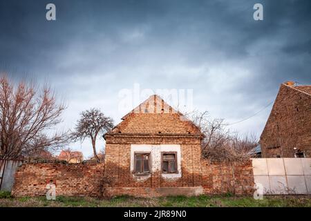 Foto di una fattoria abbandonata in Vojvodina, in Serbia, con la facciata della sua casa principale gravemente danneggiata e decadente. Foto Stock