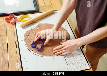 Vista delle mani delle donne che cucinano biscotti fatti in casa da un impasto di pan di zenzero arrotolato con formine culinarie Foto Stock