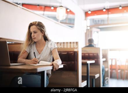 Si prepara per le finali. Una giovane studentessa focalizzata che usa il suo laptop per studiare al tavolo in un bar. Foto Stock