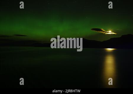 L'aurora boreale brilla con una luna che sale sulle acque del passaggio interno dell'Alaska. Foto Stock