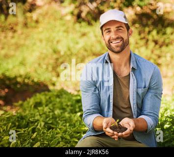 Tutto è cominciato con una piantina. Ritratto di un giovane agricoltore felice che tiene un mucchio di terreno con una piantina che cresce fuori di esso. Foto Stock