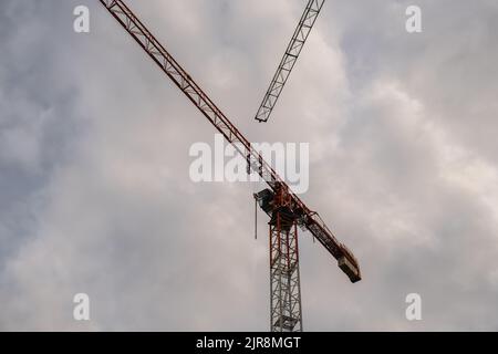 Sagome di gru edili e edificio residenziale incompiuto contro l'alba sopra la città. Edilizia abitativa, condominio costruzione di nuovi edifici residenziali. Sullo sfondo del cielo del tramonto. Foto Stock