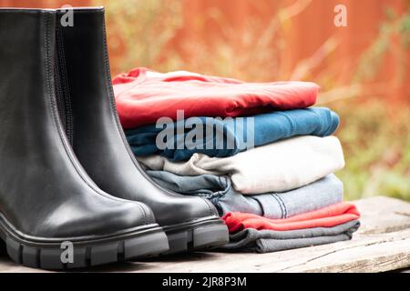 stivali neri alti da donna con suole spesse e un mucchio di cose si levano in piedi su un asse di legno al sole sulla strada, scarpe da donna e abiti invernali, fas Foto Stock