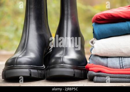 stivali neri alti da donna con suole spesse e un mucchio di cose si levano in piedi su un asse di legno al sole sulla strada, scarpe da donna e abiti invernali, fas Foto Stock