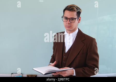 Insegnante davanti alla classe che spiega un argomento. Un uomo elegante che dà una classe. Professore universitario con un libro in mano. Foto di alta qualità Foto Stock