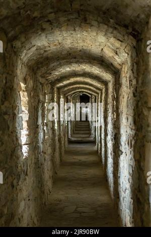 Un lungo corridoio a tunnel in pietra con finestre in un antico castello. Messa a fuoco selettiva. Foto Stock