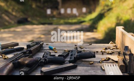 Numerosi cannoni, fucili e proiettili di munizioni posizionati su un tavolo di legno vicino al poligono di tiro. Gamma di pistole per esterni. Nessuna gente. Foto di alta qualità Foto Stock