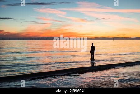 Una silhouette di una statua di Iron Man al tramonto sulla spiaggia di Crosby vicino a Liverpool vista sul Mare d'Irlanda nell'agosto 2022. Foto Stock