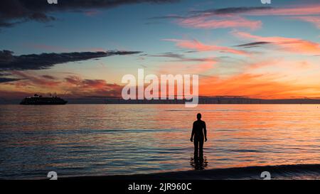 Un solo Iron Man guarda la nave da crociera World Navigator passando dalla spiaggia di Crosby al tramonto dopo la sua prima visita a Liverpool nell'agosto 2022. Foto Stock