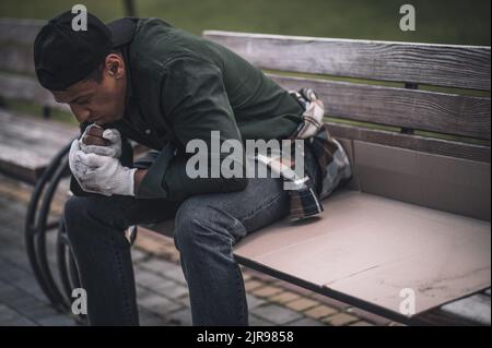 Uomo seduto accovacciato sulla panca nel parco Foto Stock