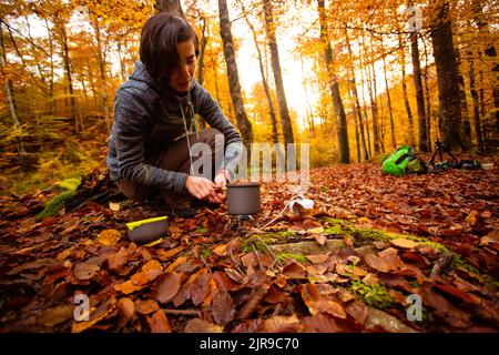 La donna usa un riscaldatore a gas portatile e una padella per cucinare all'aperto Foto Stock