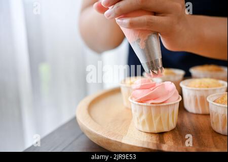 Colpo corto di giovane donna usando il sacchetto della stretta della crema per decorare il cupcake, fare il cupcake Foto Stock