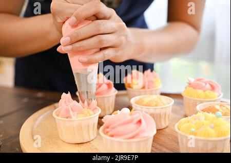 Colpo corto di giovane donna usando il sacchetto della stretta della crema per decorare il cupcake, fare il cupcake Foto Stock