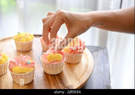 Un panettiere femminile che decora il suo bel cupcake fatto in casa con una piccola palla di cioccolato bianco. Immagine della mano di primo piano Foto Stock