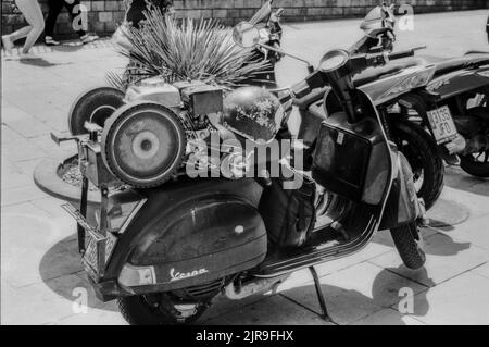 Una foto in scala di grigi di uno scooter Vespa italiano parcheggiato in strada Foto Stock