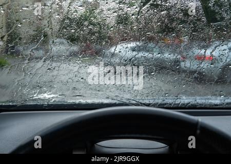 Gocce di pioggia sfocate sul parabrezza dell'auto. Il conducente è nel traffico in una giornata nuvolosa, con cattive condizioni atmosferiche durante una tempesta. Il pericolo di guida Foto Stock