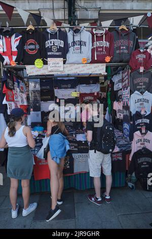 Turisti che acquistano T-shirt al mercato di Covent Garden a Londra in estate Foto Stock