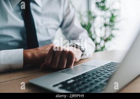 Uomo d'affari con pugni appicciato alla scrivania dell'ufficio di fronte al computer portatile. Le dita arricciate nel pugno sono di solito segno di ansia e frustrazione. Selez Foto Stock